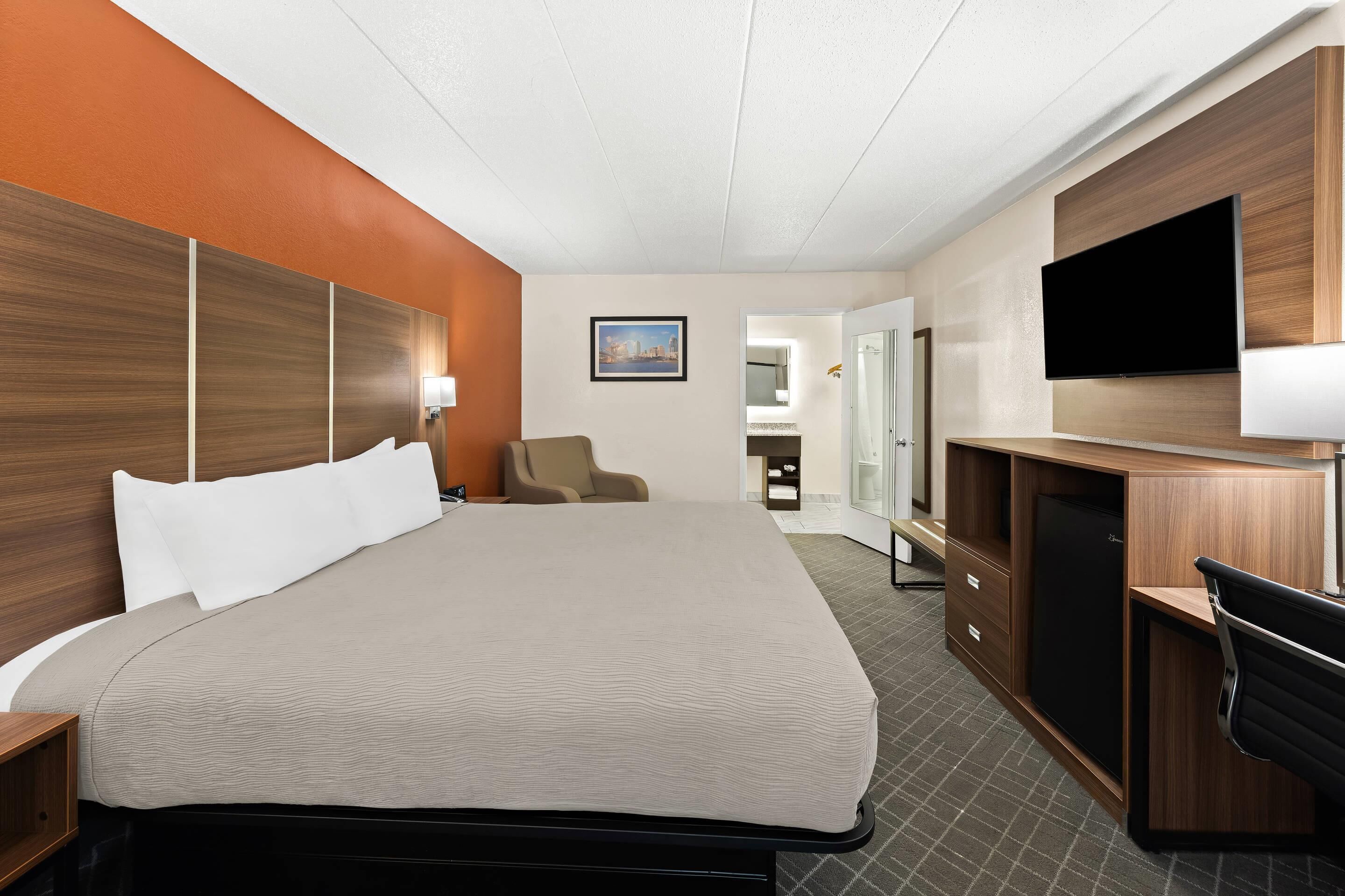 A hotel room with a large bed, a desk with a chair, a television, and a bathroom visible through an open door.