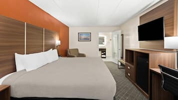 A hotel room with a large bed, a desk with a chair, a television, and a bathroom visible through an open door.