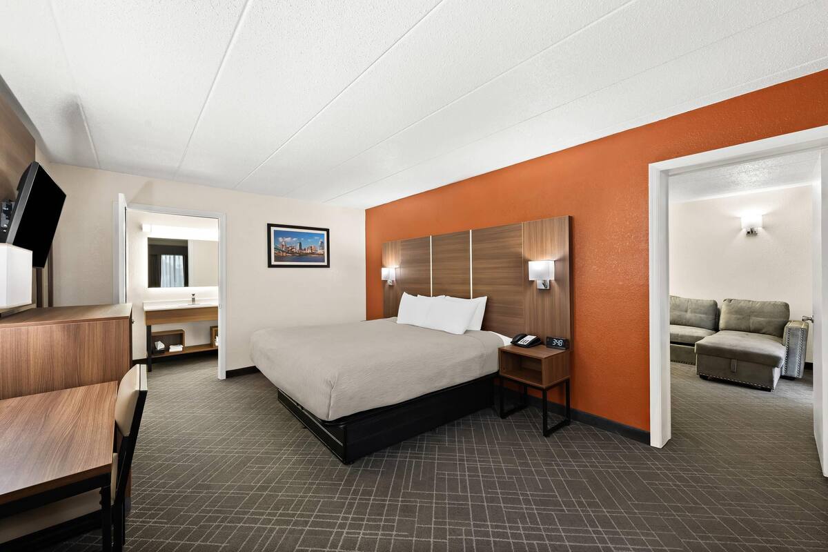 A hotel room with a bed, bedside table, lamp, and a view of a cityscape.