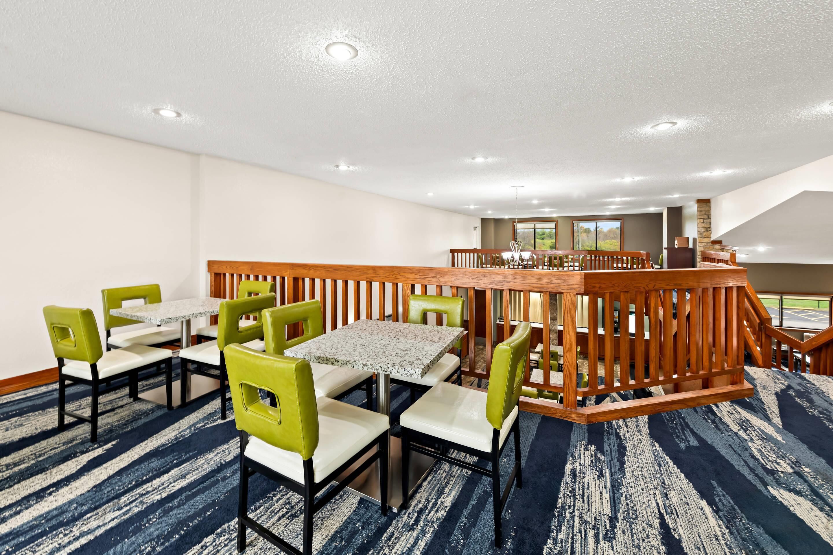Un espace de restauration d’hôtel doté d’une rambarde centrale en bois, de plusieurs tables et chaises, et offrant une vue sur l’extérieur grâce à de grandes fenêtres.