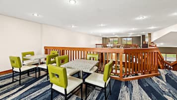 Un espace de restauration d’hôtel doté d’une rambarde centrale en bois, de plusieurs tables et chaises, et offrant une vue sur l’extérieur grâce à de grandes fenêtres.