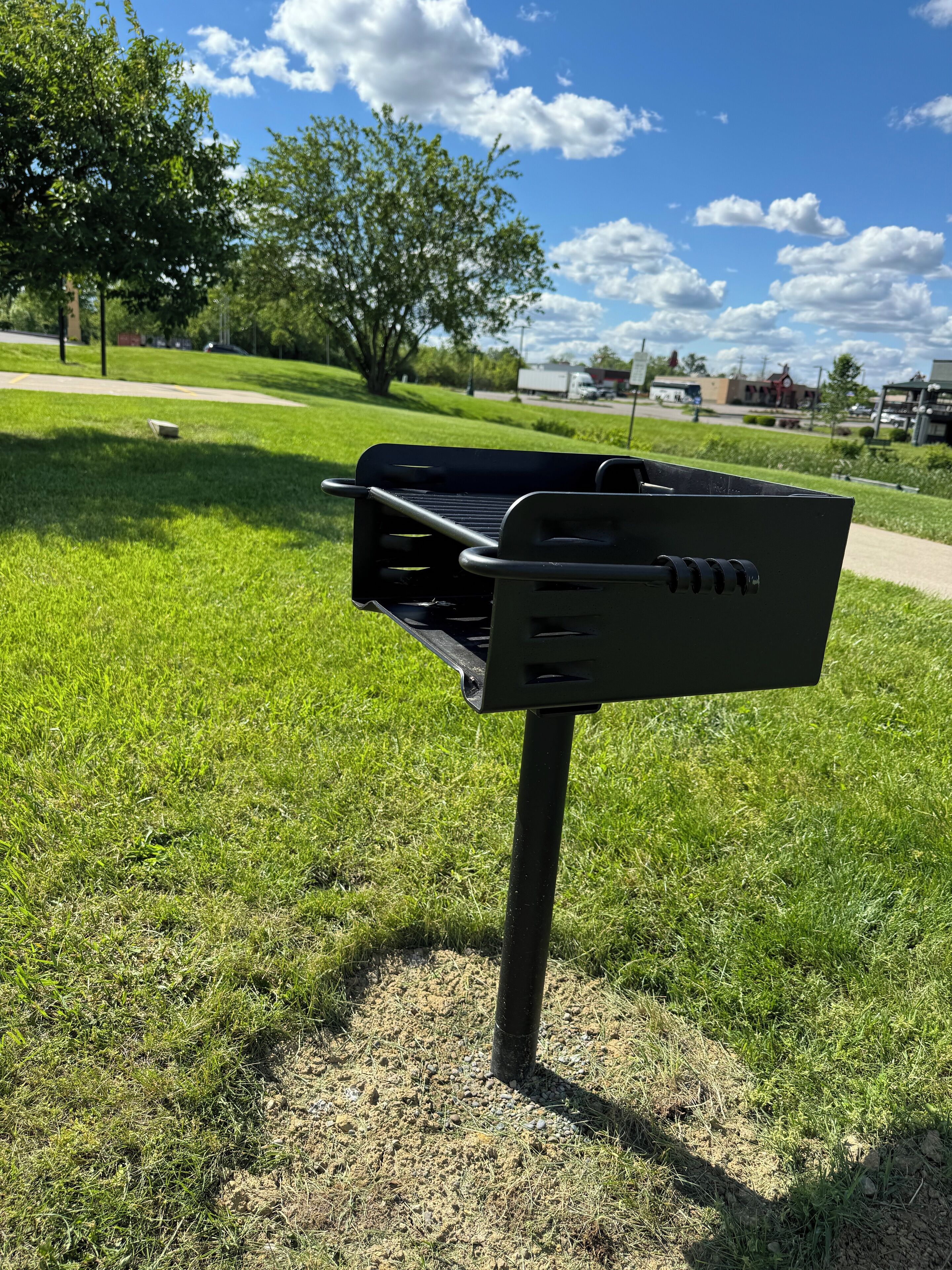 A portable grill on a grassy area with a clear sky and trees in the background.