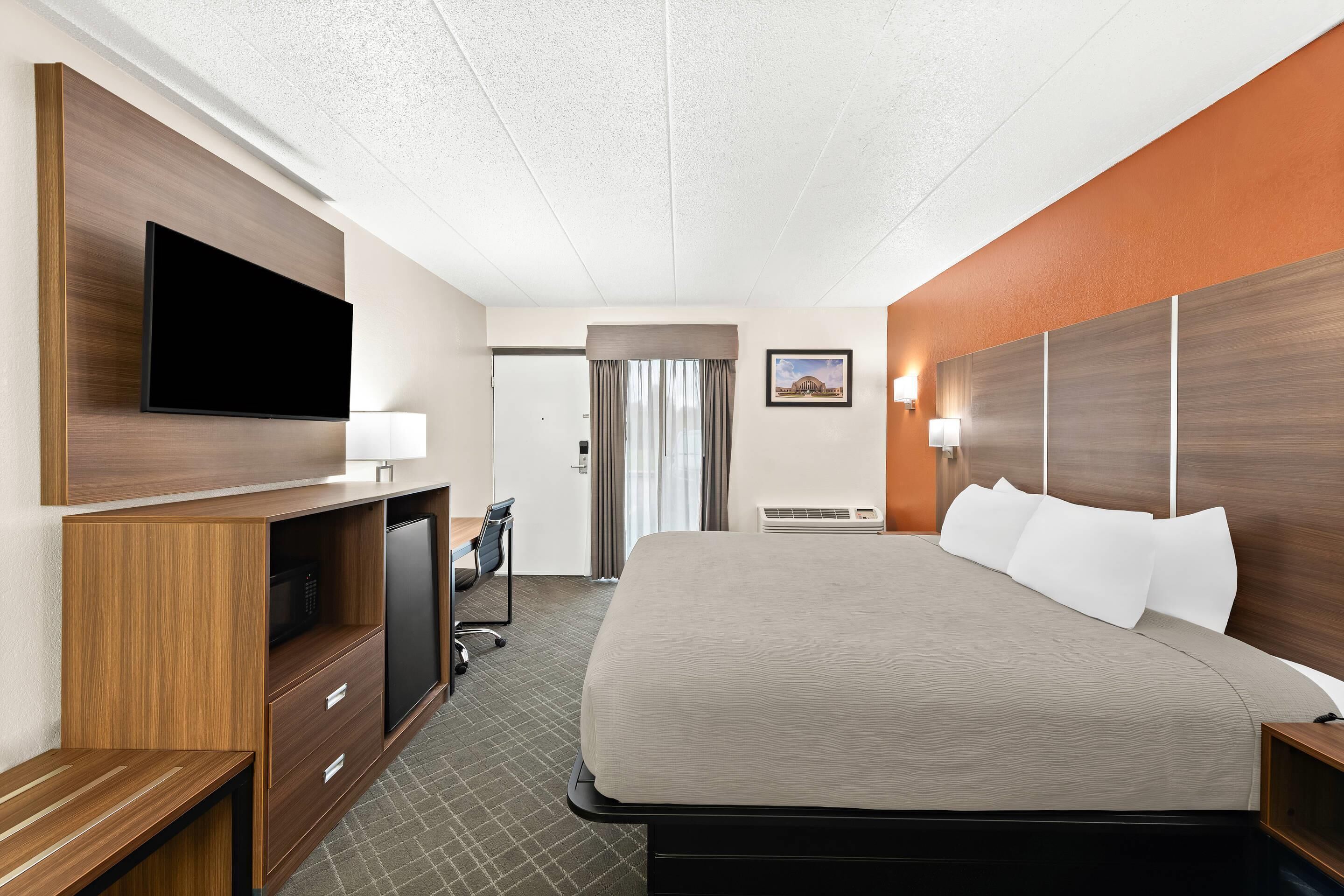 Une chambre d’hôtel avec un grand lit, un téléviseur à écran plat, un bureau avec une chaise et une fenêtre avec des rideaux.