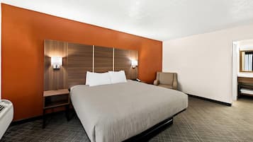 A hotel room with a large bed, a nightstand, a chair, and a desk with a lamp.