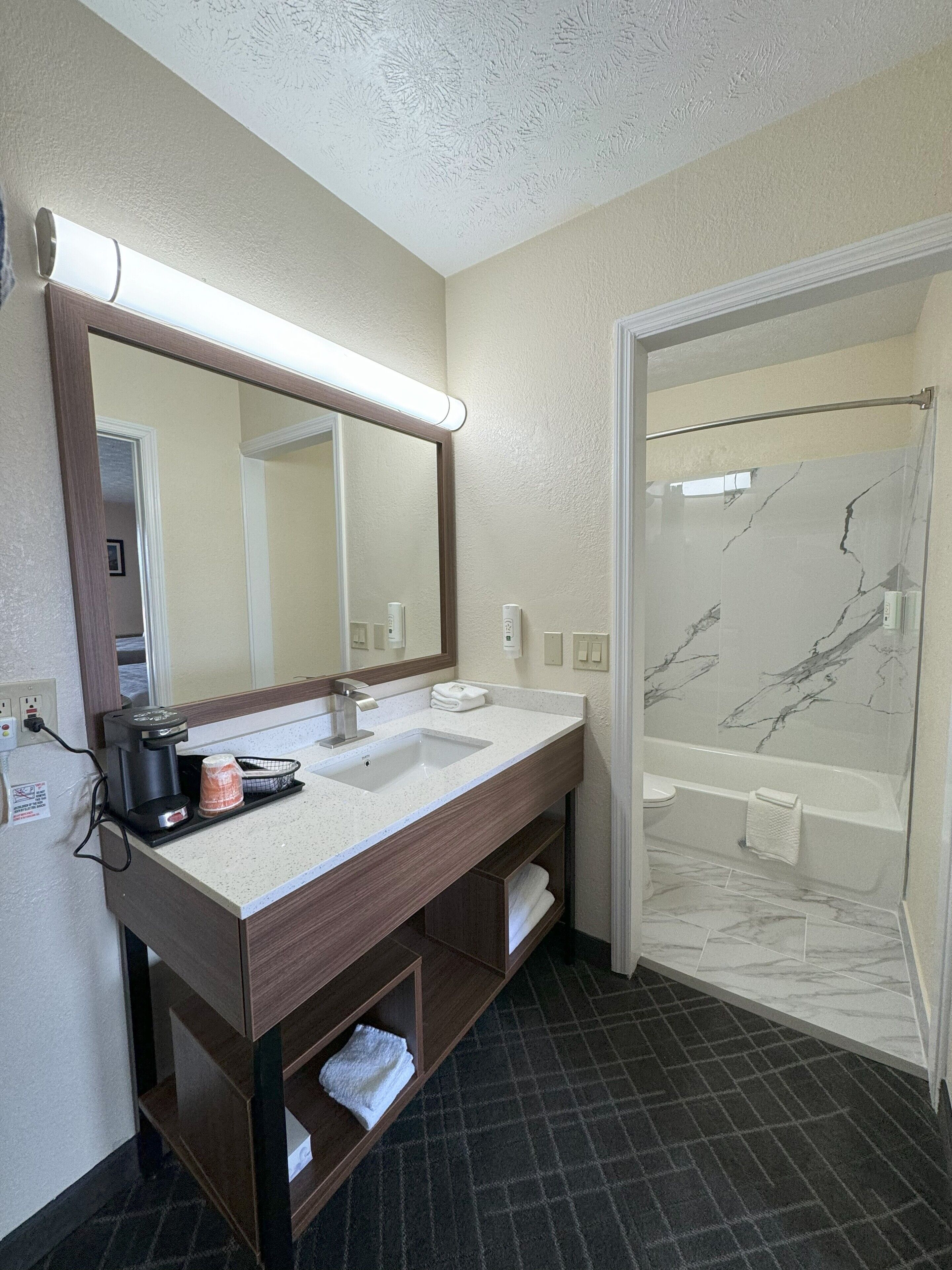 A bathroom with a large mirror, a sink, a shower, and a towel rack.