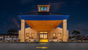 A hotel entrance with a blue roof and beige walls, a sign indicating 'Quality Suburban', and a parking lot with directional arrows. - Quality Inn Mason Near Kings Island (Mason)