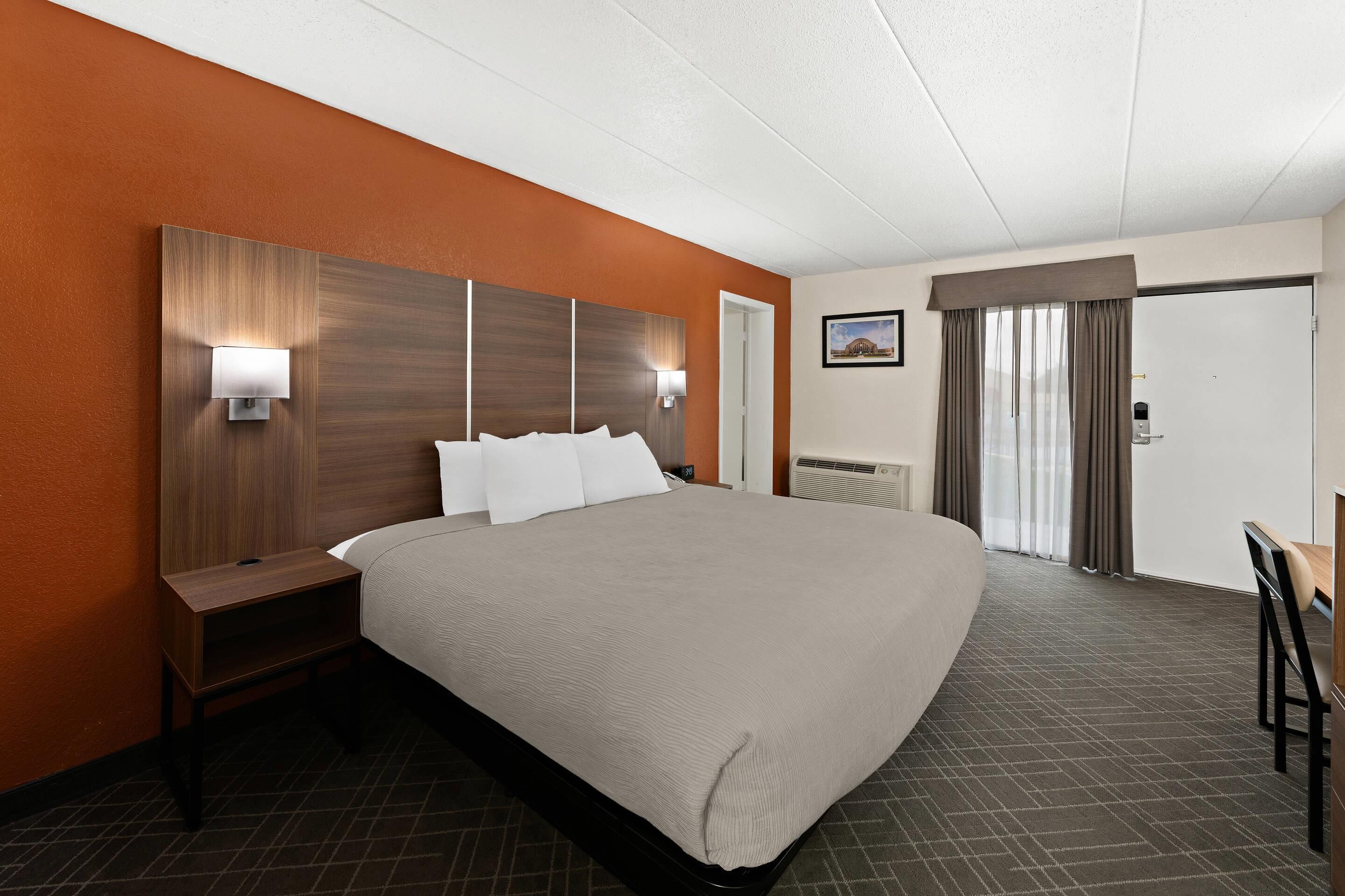 Een hotelkamer met een groot bed, een bureau en een stoel. Er is een nachtkastje, een wandlamp en een schilderij aan de muur.