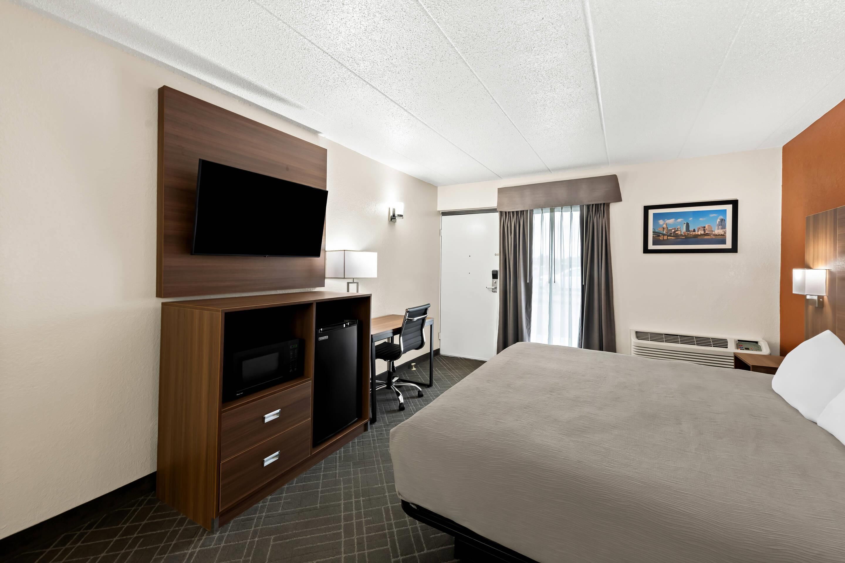 Une chambre d’hôtel avec un grand lit, un bureau avec une chaise, une télévision, un petit réfrigérateur et un tableau au mur.