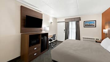 Une chambre d’hôtel avec un grand lit, un bureau avec une chaise, une télévision, un petit réfrigérateur et un tableau au mur.