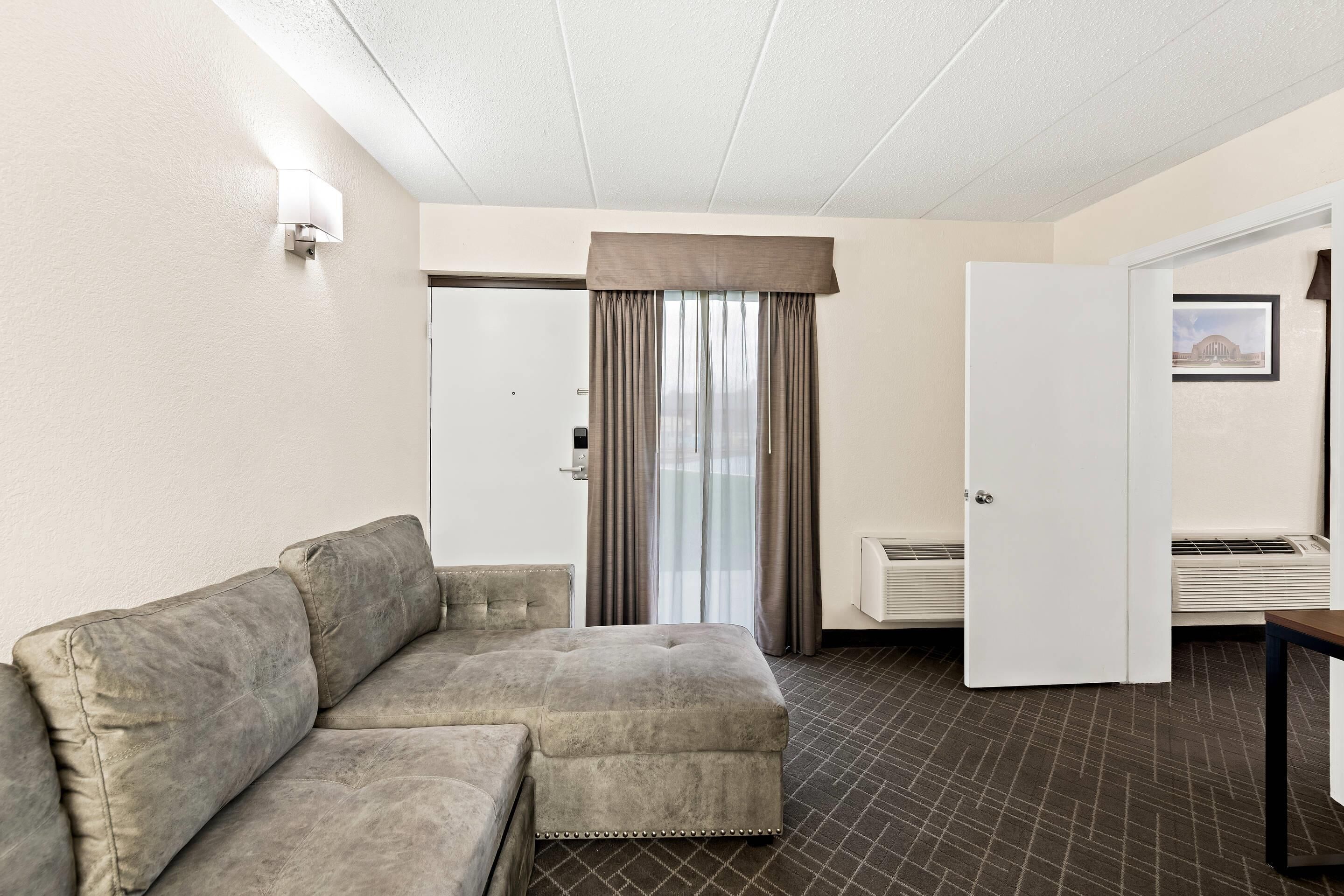 Habitación de hotel con sofá modular, una puerta, ventana con cortinas y un radiador.