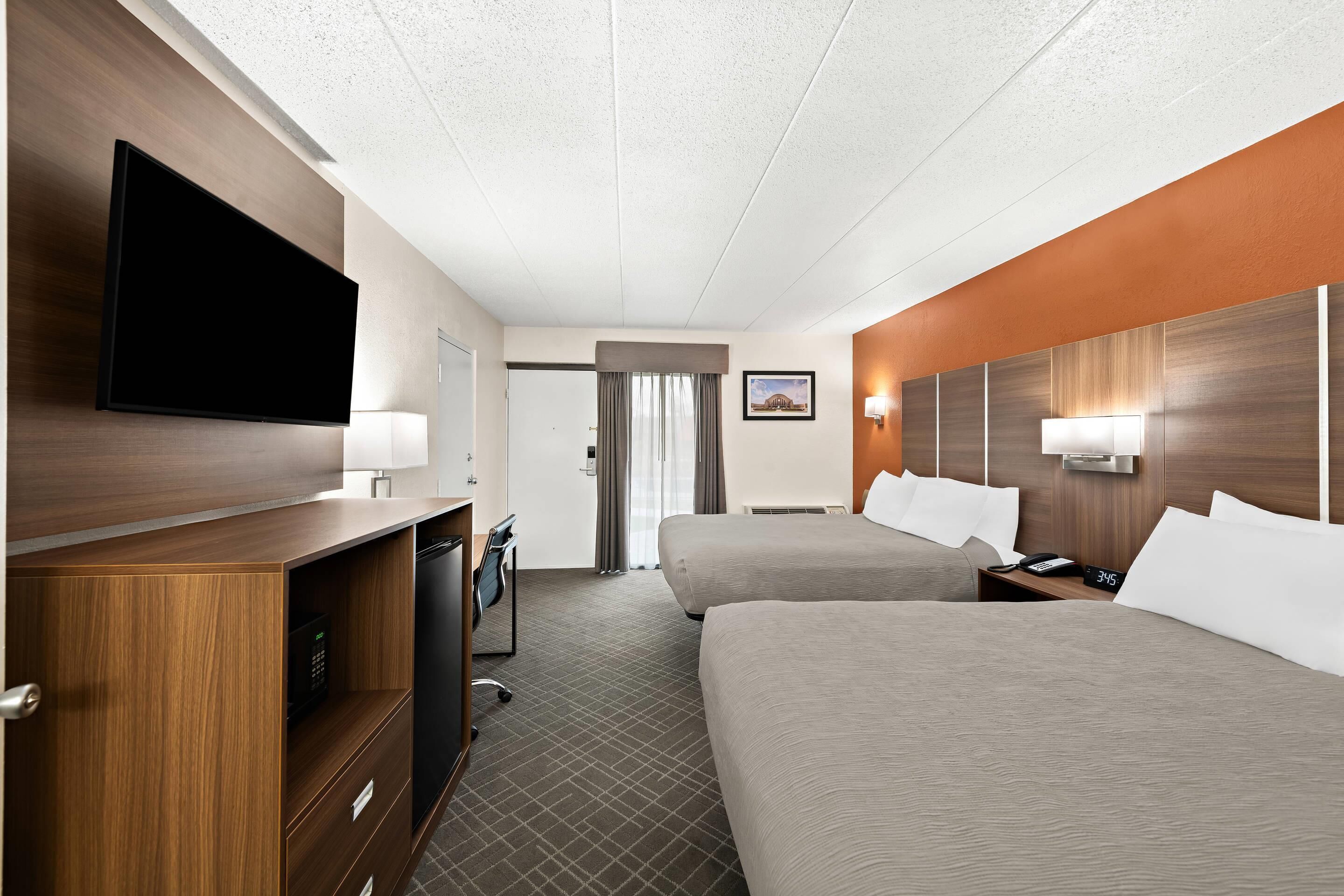 Een hotelkamer met twee bedden, een flatscreen televisie, een bureau met lamp en een deur naar een badkamer.