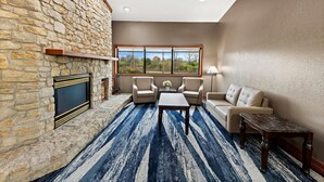 A living room with a stone fireplace, a large window, a blue striped rug, a sofa, and two armchairs. - Quality Inn Mason Near Kings Island (Mason)