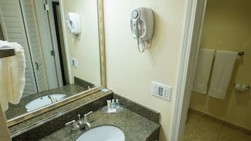A bathroom with a granite countertop sink, a mirror, a hairdryer, and a trash can.