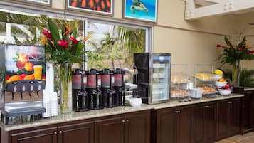 Zona de bufé con estación de café, un refrigerador y diversas opciones de comida.