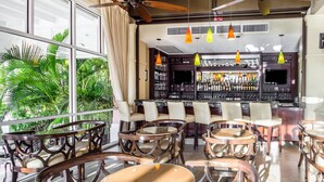 Un área de bar con mesas y sillas redondas, un televisor y una barra repleta de botellas.