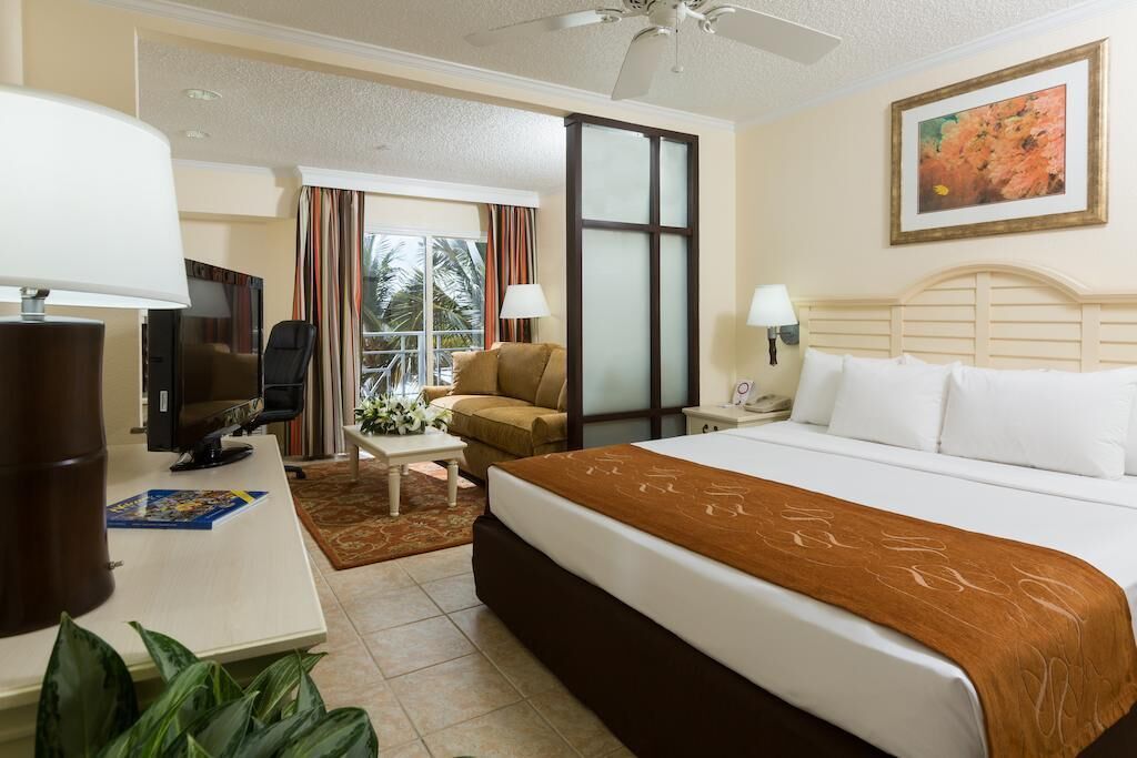 A hotel room with a bed, a desk with a TV, a chair, a window with curtains, and a ceiling fan.