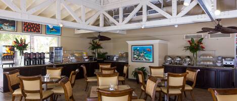 A spacious dining area with high ceilings and a kitchen in the background.