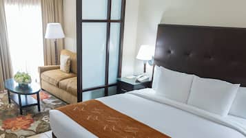 Una habitación de hotel con una cama grande, un sofá, una mesita con una lámpara y una mesita de noche con teléfono.