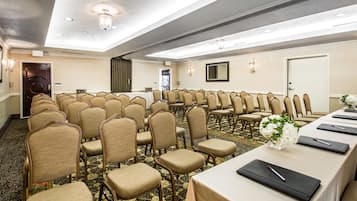 A conference room with rows of beige chairs, a long table with black placemats and pens, and a floral centerpiece.