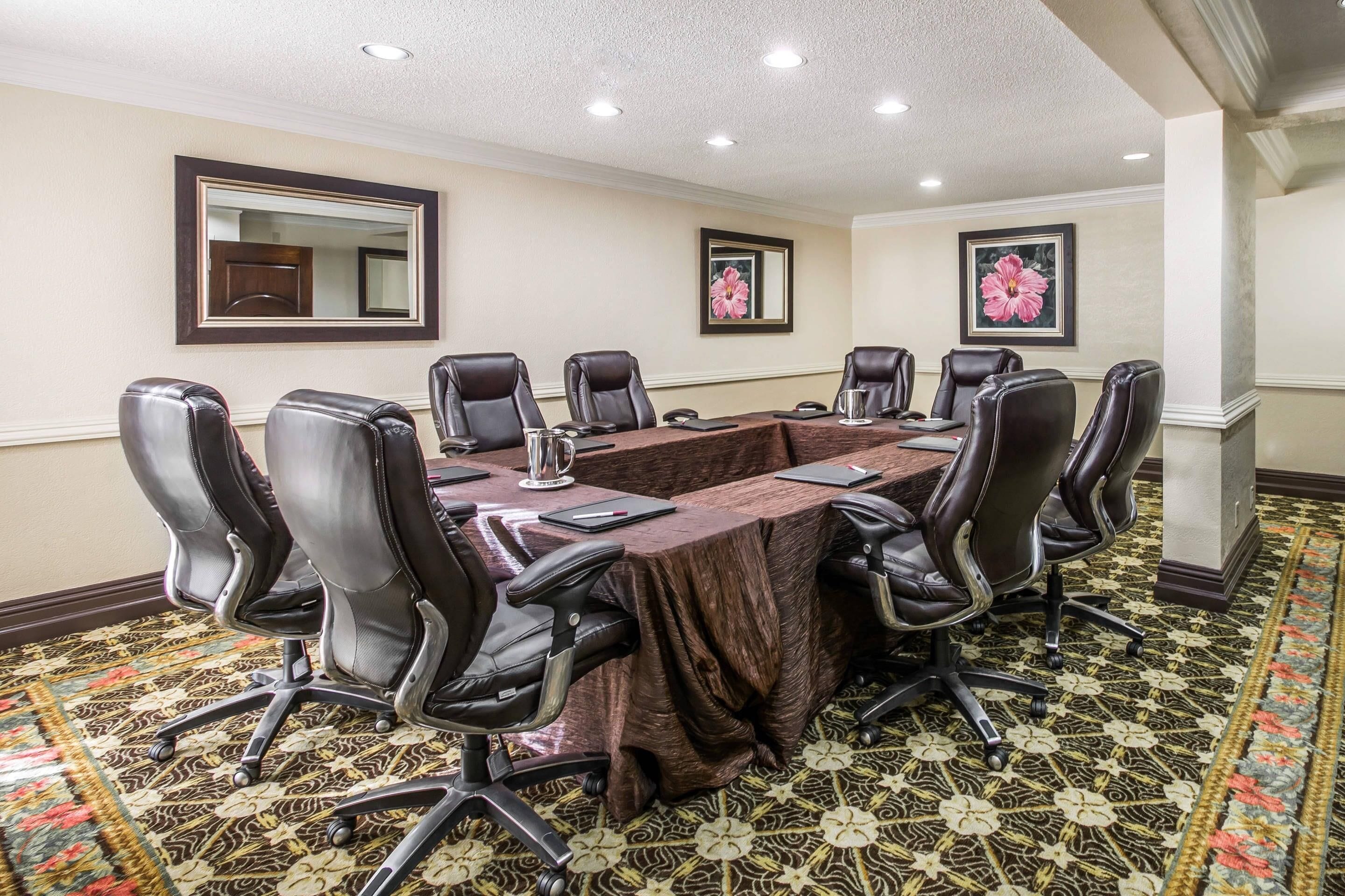 A conference room with a long table, eight chairs, and a patterned carpet.