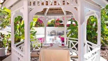 A white gazebo with a table and chairs set up underneath, surrounded by lush greenery.