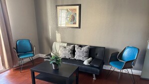 Ein Wohnzimmer mit einem schwarzen Sofa, zwei blauen Sesseln, einem schwarzen Couchtisch und einem gerahmten Bild an der Wand.