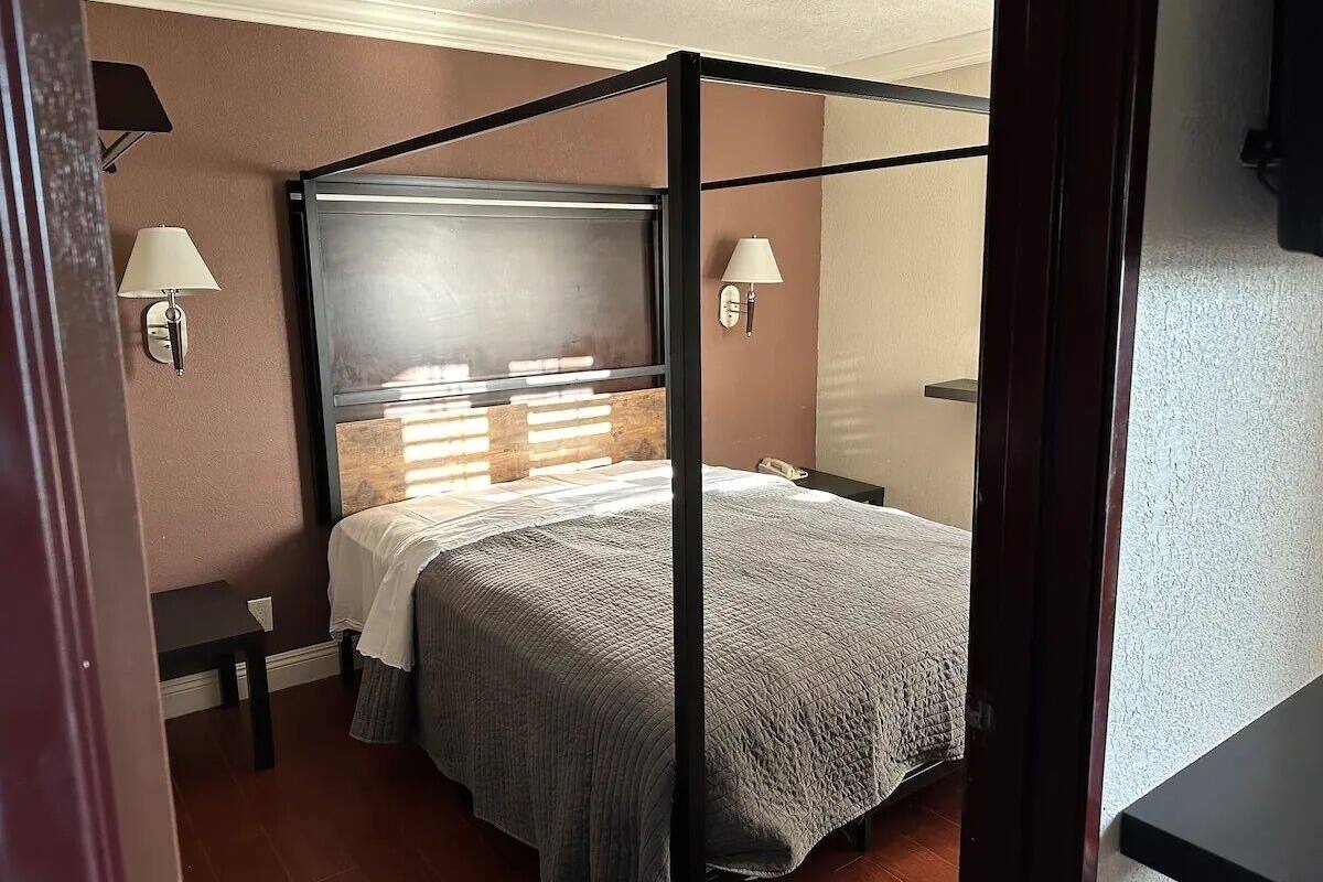 A four-poster bed with a grey bedspread in a room with beige walls and a wooden floor.
