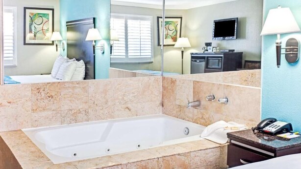 Ein modernes Badezimmer mit einer großen Badewanne, einem Waschtisch mit Spiegel und einem an der Wand befestigten Flachbildfernseher.