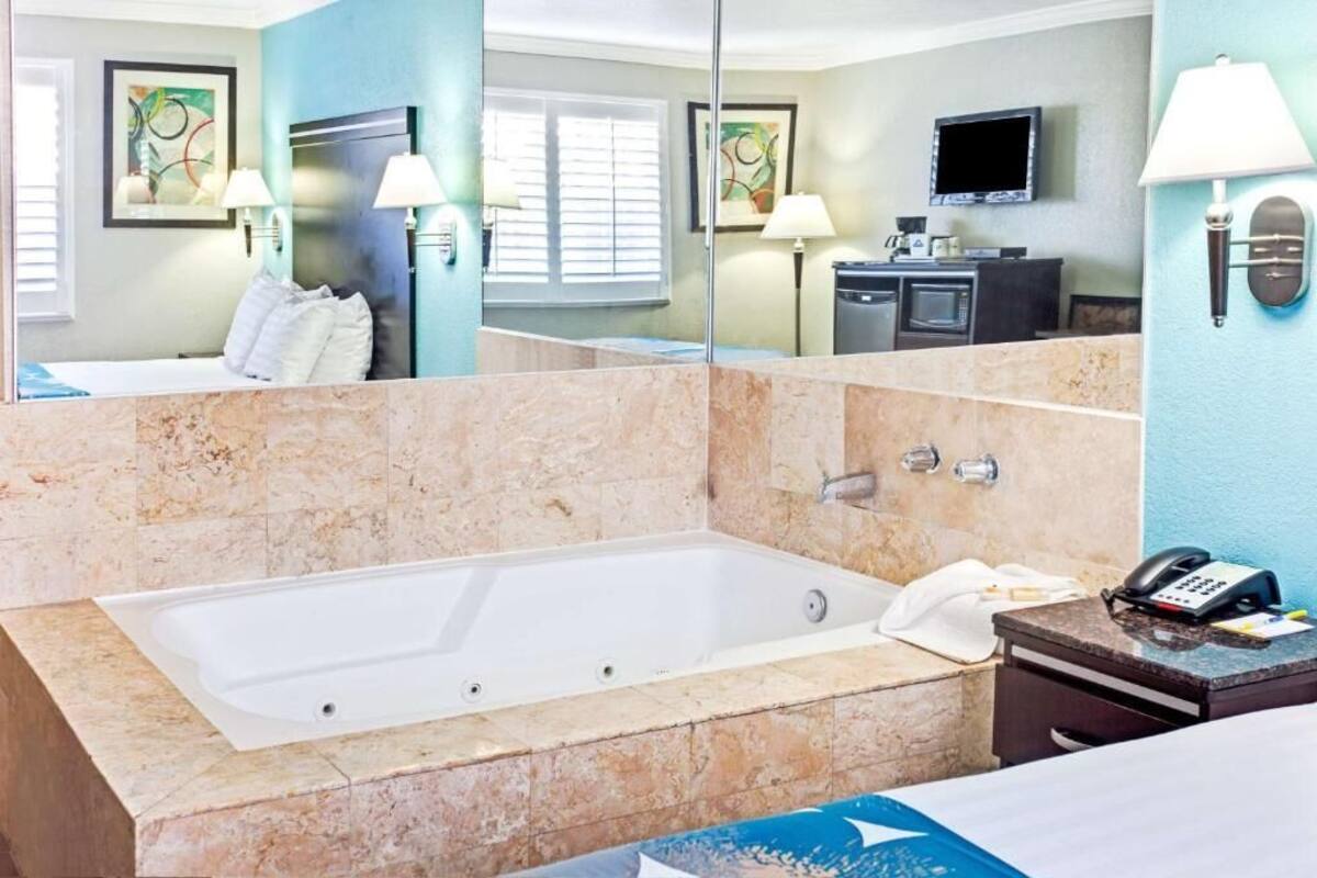 A modern bathroom with a large bathtub, a vanity with a mirror, and a flat-screen TV mounted on the wall.