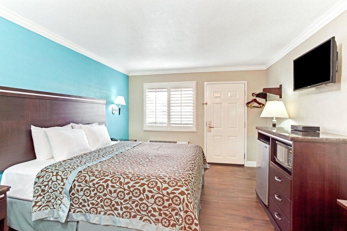 A hotel room with a bed, a desk with a lamp, a TV, and a door.