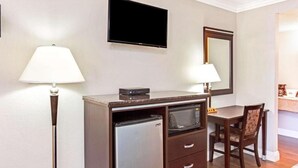Ein kompaktes Hotelzimmer mit Küchenzeile, einem Flachbildfernseher, einem Spiegel und einem Schreibtisch mit Stuhl.