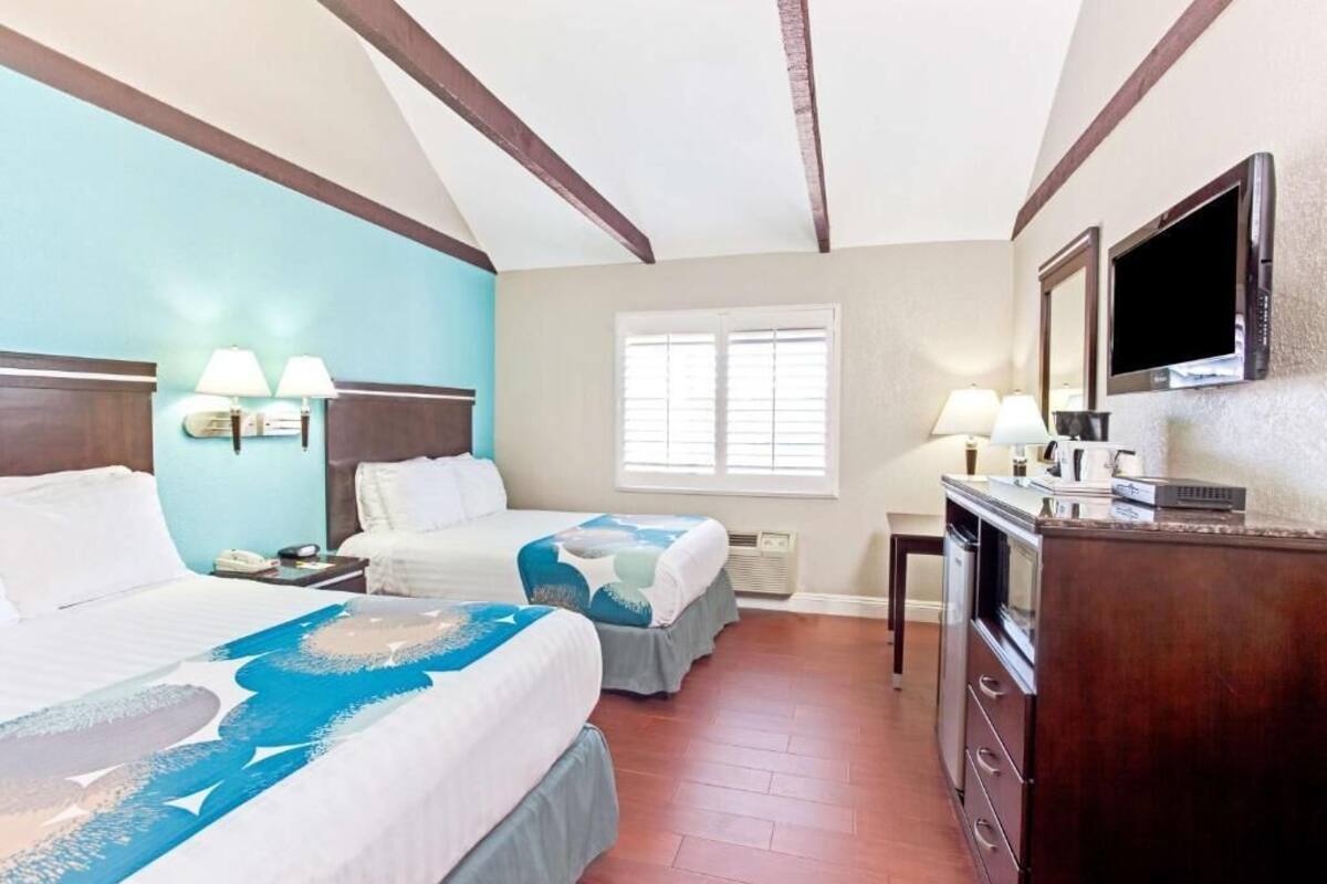 A hotel room with two beds, a TV, a desk with a lamp, and a window with blinds.