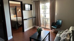Ein Wohnzimmer mit einer Couch, einem Couchtisch mit einer Pflanze, einem Fernseher und einer Glastür, die auf einen Balkon führt.