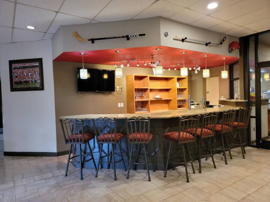 A bar area with multiple stools, a television mounted on the wall, and shelves with glasses.
