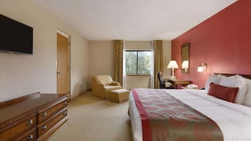 A hotel room with a bed, a wooden dresser, a chair, a desk, a lamp, and a TV.