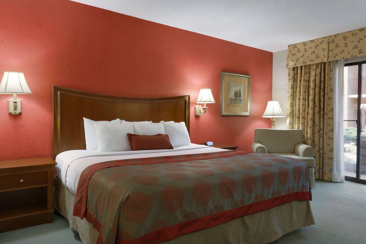A hotel room with a large bed, two bedside lamps, a chair, a desk, and a window with curtains.