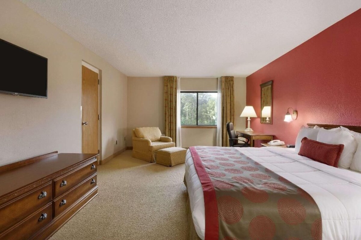 A hotel room with a bed, a chair, a desk, a television, and a window with curtains.