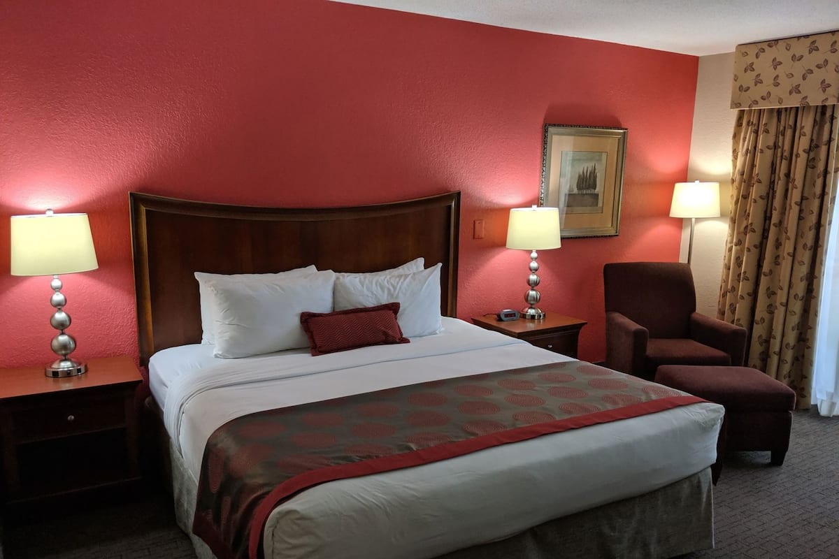 A hotel room with a large bed, two bedside tables with lamps, a chair, and a framed picture on the wall.