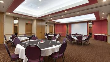 Un salón de conferencias con varias mesas, sillas y una pantalla para proyector.