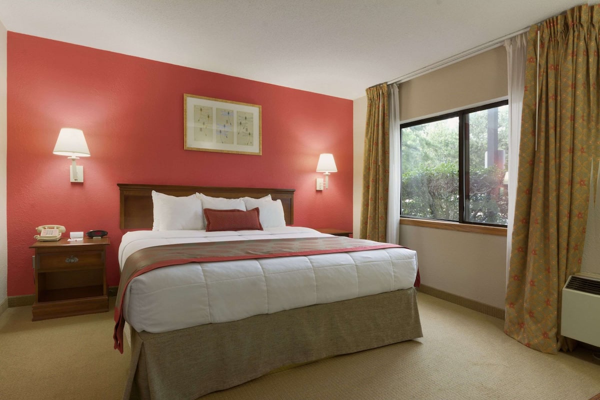 A hotel room with a large bed, two bedside lamps, a nightstand with a telephone, and a window with curtains.