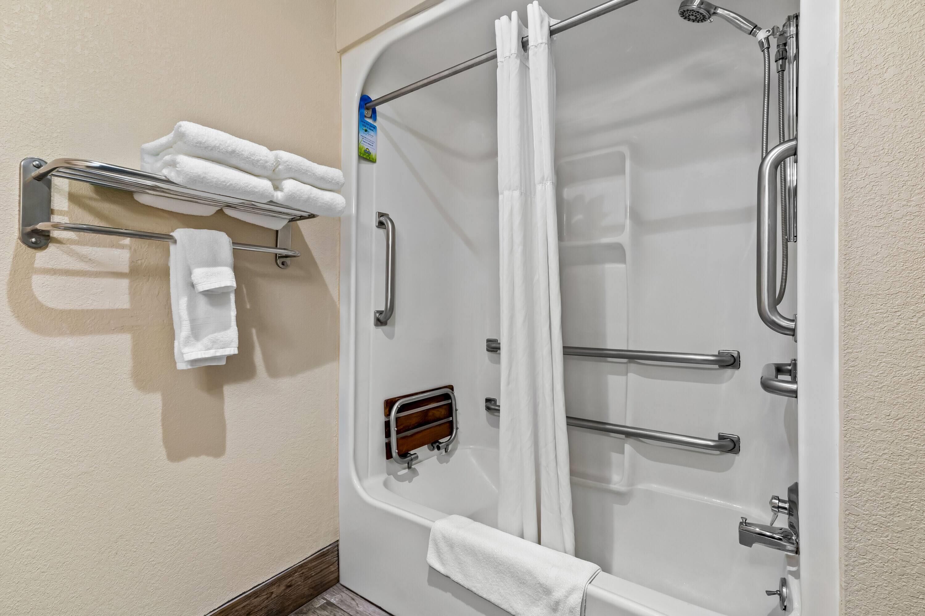 A shower with a glass door, a towel rack with folded towels, and a handheld showerhead.