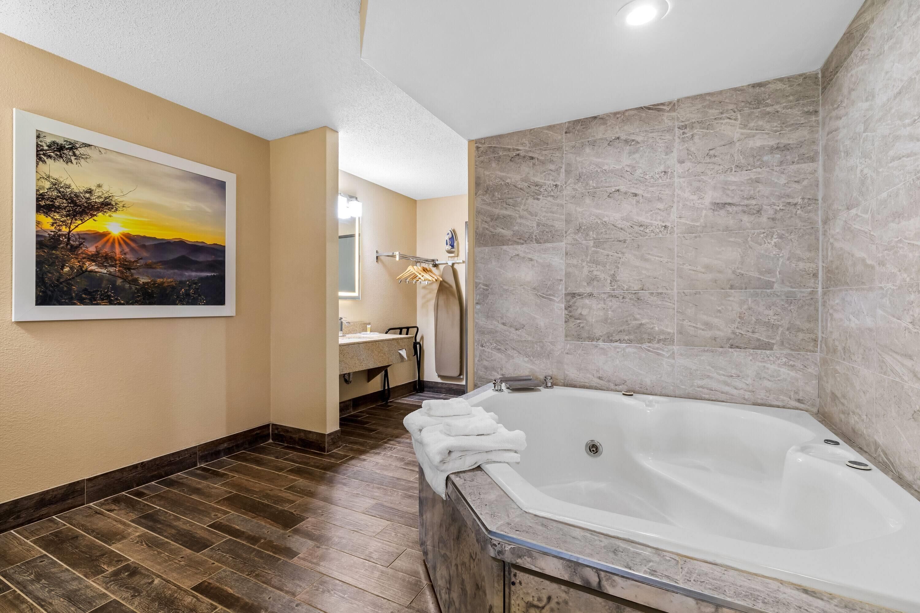 Une salle de bain moderne avec une grande baignoire, un plancher en bois, un tableau représentant un coucher de soleil et un mur en marbre.