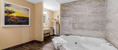 A modern bathroom with a large bathtub, a wooden floor, a painting of a sunset, and a marble wall.