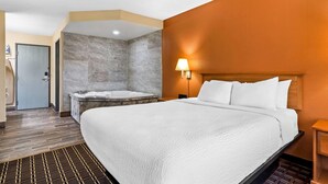 Una habitación de hotel con una cama grande, un baño con bañera y suelo de madera.