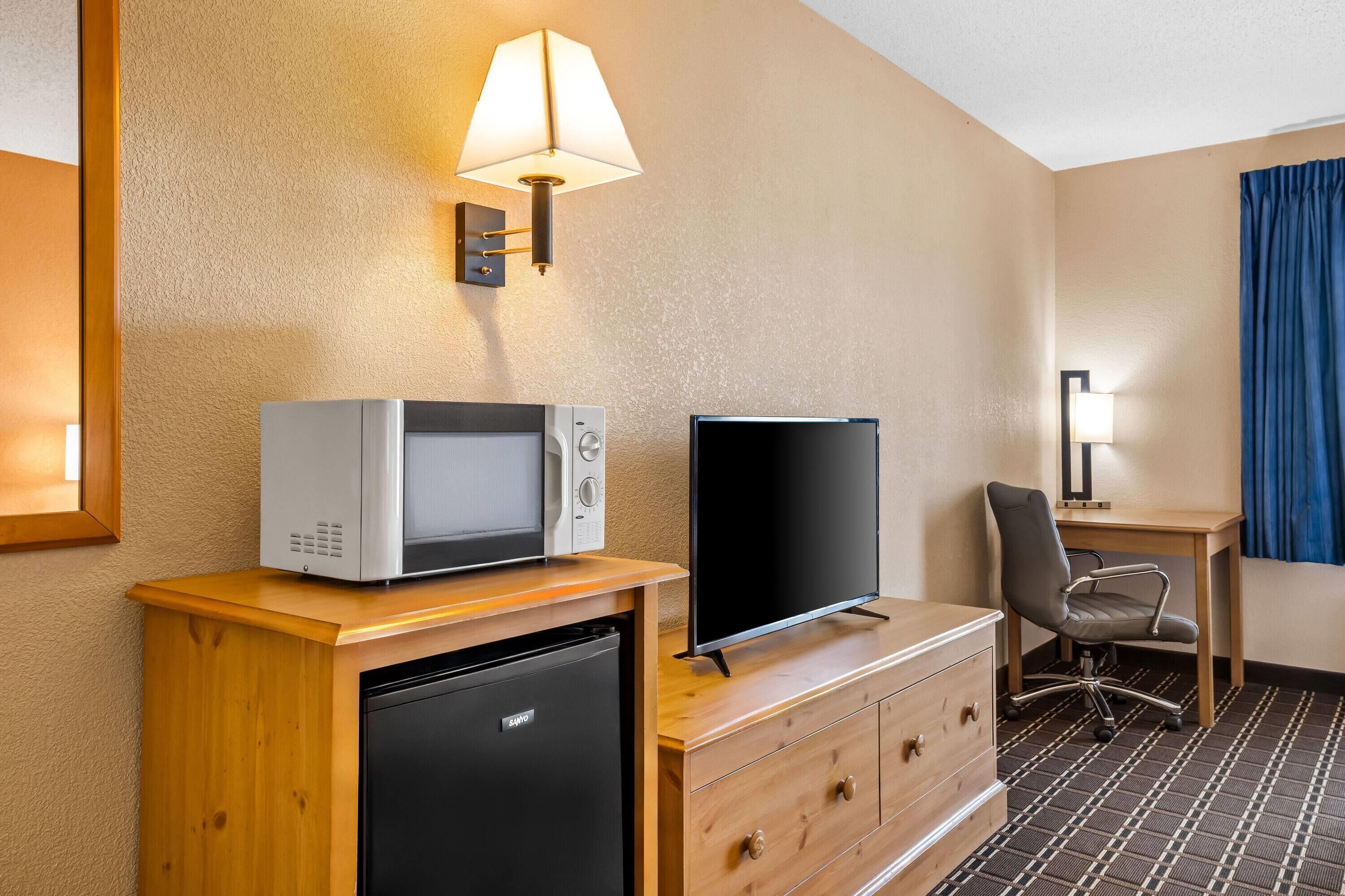 A compact hotel room with a kitchenette, a flat-screen TV, a desk, and a chair.