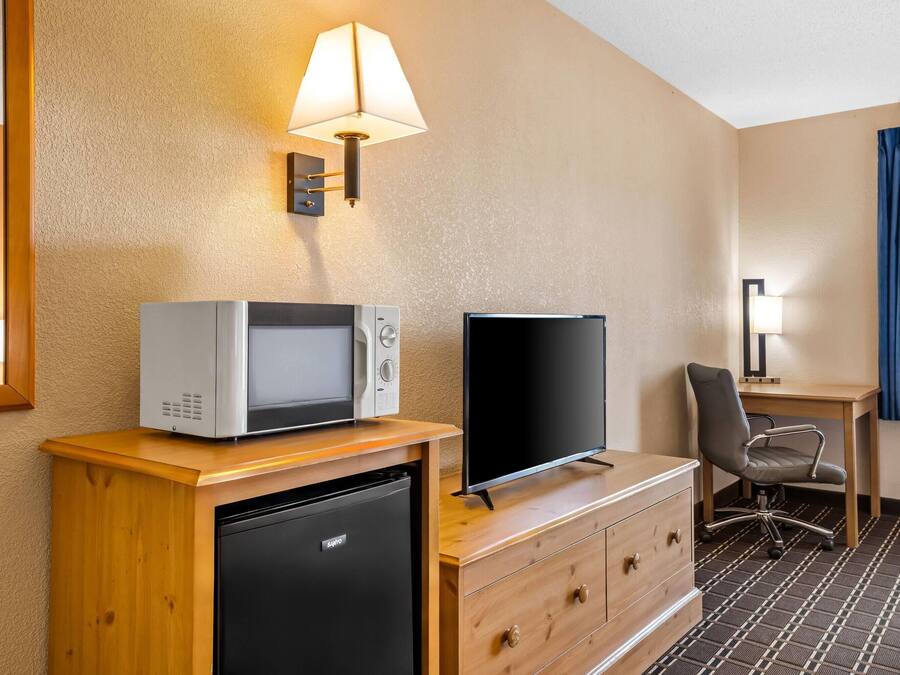A compact hotel room with a kitchenette, a flat-screen TV, a desk, and a chair.