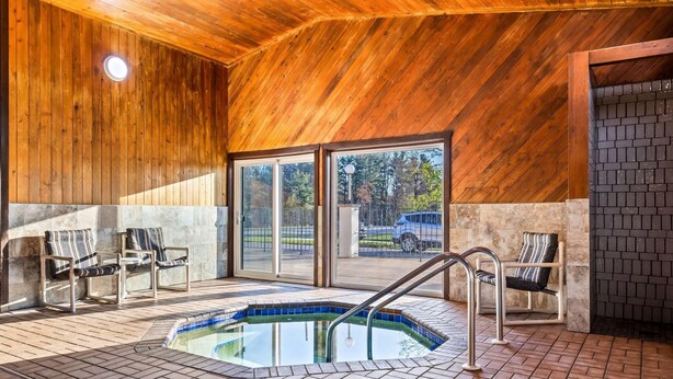 Una piscina interior con suelo de baldosas, techo de madera y dos sillas cerca de la piscina.