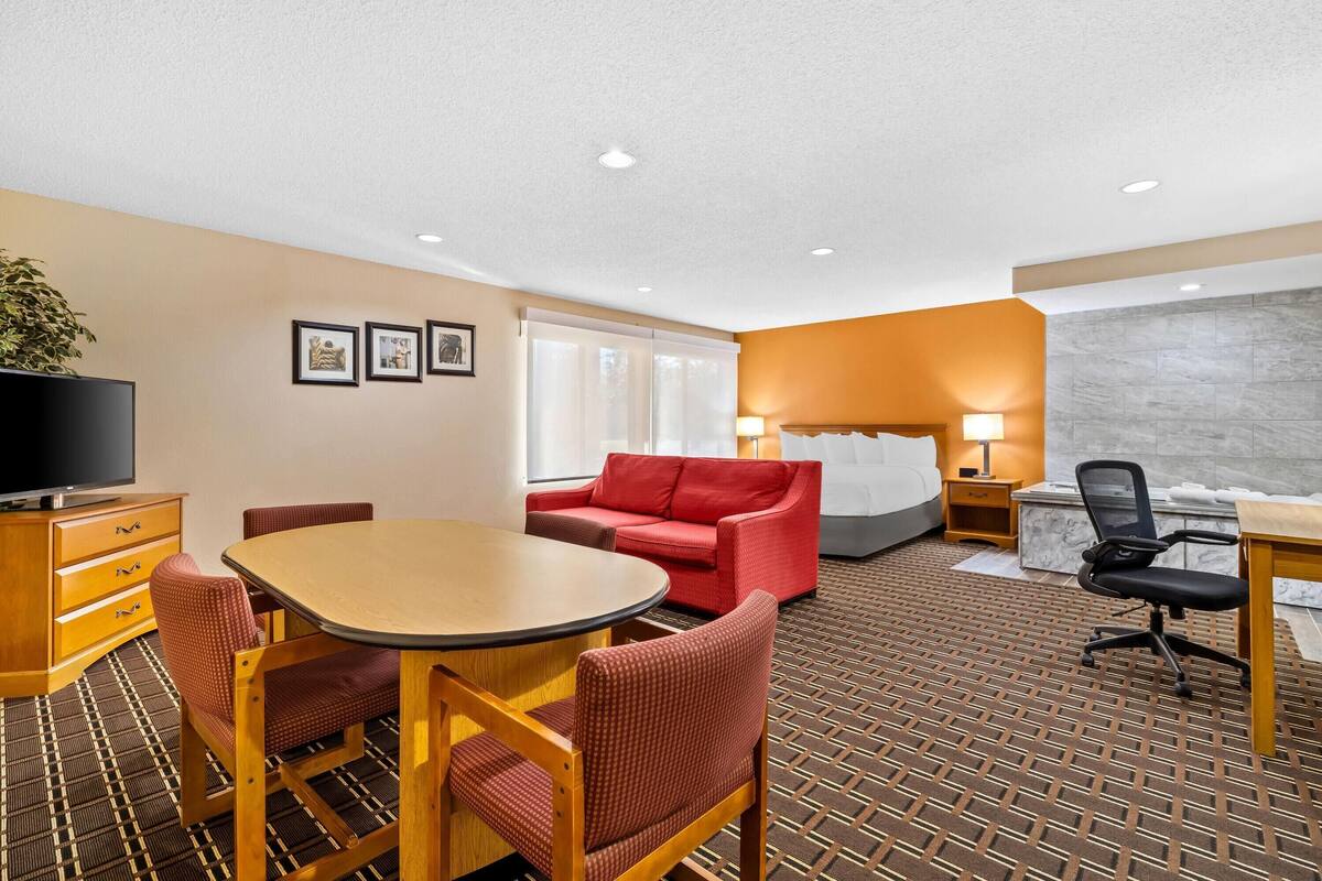 Ein Hotelzimmer mit Esstisch, rotem Sofa und einem Bett mit Kopfteil.