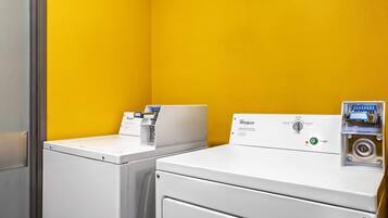 Een wasserette met twee witte wasmachines en drogers tegen een gele muur.
