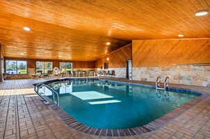Una piscina interior con techo de madera y paredes de piedra, rodeada de sillones de descanso y vistas al exterior.